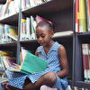 Girl Reading a Book in Front of Shelf in Library